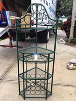 Full front view of the green metal corner wine rack showing its height and decorative scrollwork.
