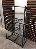 Full view of black Origami collapsible shelving unit assembled standing in storage unit, showing four wire shelves and frame.