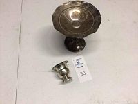 Photo showing the sterling silver pedestal dish and egg cup on a white table from a front angle, displaying overall shape and size.