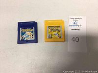 Two Game Boy Color Pokemon game cartridges side-by-side with a lot number card next to them on a white surface.