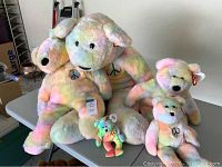 Five Ty Beanie Buddies Peace Bears of various sizes placed on a table, showing their pastel tie-dye colors and peace sign emblems.