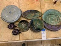Full view of stoneware covered dish with lid, two dark purple condiment servers, pottery plates and bowls arranged on tile surface.