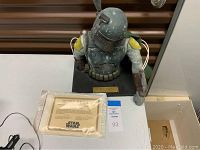 Boba Fett bust on display base with Certificate of Authenticity on table.