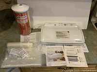 Full lot showing FoodSaver vacuum sealer with bags, canister, and instruction manuals on countertop.