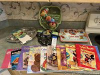Photo of pans and cake decorating books displayed on a countertop, showing the assortment including caterpillar cakelette pan and colorful book covers.