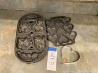 Both cast iron cakelette pans and the heart-shaped ring mold displayed on a counter.