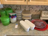 Photo showing green round plastic containers and other clear containers stacked with lids, plus white ice cream containers and red glass and plastic platters.