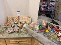 Wide view of assorted cookie cutters on table including seasonal shapes, mini pans, and cookie press discs in a clear plastic box.