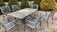 Full view of the outdoor patio set with rectangular stone top table and six cast aluminum chairs around it on a patio surface.