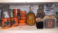 Shelf with orange votive holders and bowls, large pumpkin candle in plastic wrap, some wrapped in bubble wrap