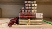 Various packaged and unpackaged candles including taper candles in red and ivory with wallpaper texture, votive candles in packaging, and two metal candle snuffers in red and silver.