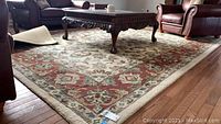 Full view of the area rug spread in a living room under a carved wooden coffee table, showing the beige and red floral design and overall condition.