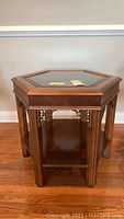 Front and top view of octagonal wood accent table with glass top insert on wood floor against white wall.