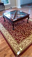 Area rug under wooden coffee table in sitting room with decorative red, beige, and floral design.