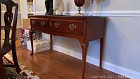 Full view of the polished mahogany sideboard serving table in a dining area, showing the front and side profile with three drawers and brass handles.