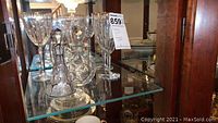 Lower shelf showing two mismatched crystal decanters (round and slender) with stoppers alongside stacked small plates