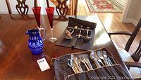 Full view of all items including blue etched glass pitcher, two red etched Lenox champagne flutes, and Royal Albert flatware laid out on table.