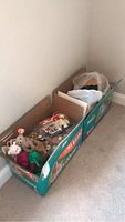 Three open cardboard boxes containing assorted Beanie Babies with original tags, positioned against a white wall on beige carpet.