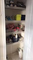 White wire shelves inside bathroom closet showing boxed lightbulbs, handbags, personal care containers, and miscellaneous items