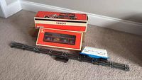 Lionel flatbed truck with trailer and two boxed Lionel train cars on carpeted floor.