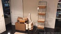 Full view of storage rack with four wicker baskets. Includes additional baskets and drawer liner rolls nearby in cardboard box.