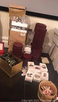Stacked boxes containing the Hallmark lighthouse ornaments, various red fabric storage boxes, and multiple white boxed ornaments on the floor along with a cylindrical container.