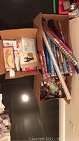 Overhead shot of two boxes showing greeting cards and rolls of wrapping paper along with ribbons.