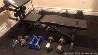 Overview of adjustable bench with preacher curl and leg extension attachments and multiple dumbbell sets arranged on floor