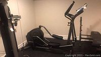 Side view of the Life Fitness elliptical trainer in a finished basement room showing the frame and flywheel housing