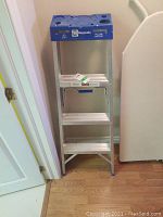 Front view of Reynolds aluminum step ladder showing three wide steps and blue top platform with tool slots.