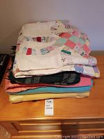 Stack of Handmade quilt and four blankets on wooden surface showing varied colors and materials.