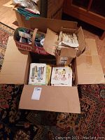Overview photo showing multiple cardboard boxes containing sewing pattern envelopes, some patterns with visible illustrated front covers.