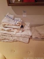 Stack of white and cream lace tablecloths and doilies shown folded on a yellow upholstered couch.