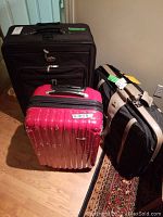 Three luggage pieces: black Air Canada soft sided rolling suitcase, red Samsonite hard sided rolling suitcase, and black and beige Samsonite soft sided rolling suitcase arranged on hardwood floor and near a wall outlet.