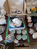 Photo showing the Spode tea pot and cup inside a cardboard box, along with other ceramic items on the table