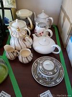 Full assortment of tea pots, sugar, creamer, and butter dish laid out on table.