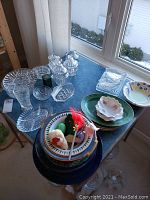 Overview of glass and ceramic serving dishes on a table by window showing variety of clear glass and ceramic bowls and plates