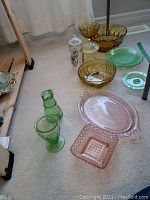 Overall view of the Depression Glass set on carpet, showing various items including pink chip and dip dish, green and amber glass candy dishes, pitchers, and platters.