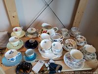 Overview of assorted fine china tea cups and saucers with a white ceramic pitcher and Bunnykins bowl