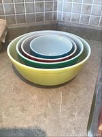 Nested set of four Pyrex mixing bowls in yellow, green, red, and light blue colors on kitchen counter.