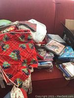 Various folded and stacked aprons, napkins, and towels piled on a red couch showing colorful patterned fabrics