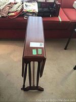 Full view of the closed mahogany drop leaf table with swivel legs and casters, showing top and side profile.