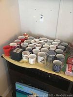 Overview of various tea and coffee mugs spread out on a surface, including a boxed kitty mug and several different ceramic mugs.