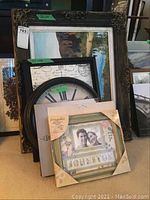 Front view showing all items in the lot including the large framed oil painting, round wall clock, personalized frame, and multiple prints.