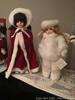 Two Christmas-themed dolls displayed on a surface, one in red dress and the other in white furry outfit
