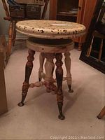 Side view showing overall stool structure, round top, turned legs with paint wear and metal feet caps.