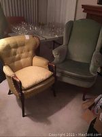 Two vintage armchairs: wood framed gold fabric fireside chair on left and green velour wingback chair on right