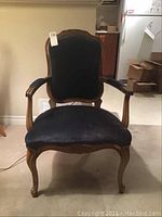 Front view of the wooden fireside chair showing full structure, scrolled wood frame, and blue velour upholstery on seat, backrest, and armrests.