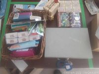 Overview of lot with basket containing tissues and wipes, boxed soap, decorative boxes, and cash box on table.