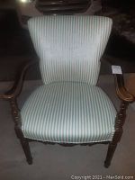 Front view of the vintage chair showing striped green and white cloth upholstery and wooden armrests.